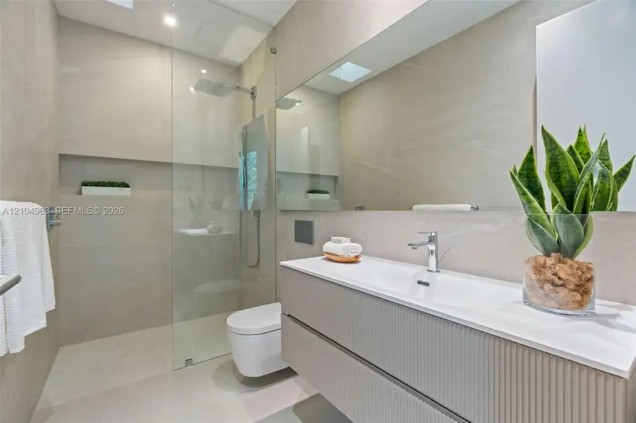 Modern bathroom featuring a textured floating vanity, integrated rectangular sink, wall-to-wall mirror, glass-enclosed walk-in shower with a rain-style showerhead, and neutral-toned wall tiles
