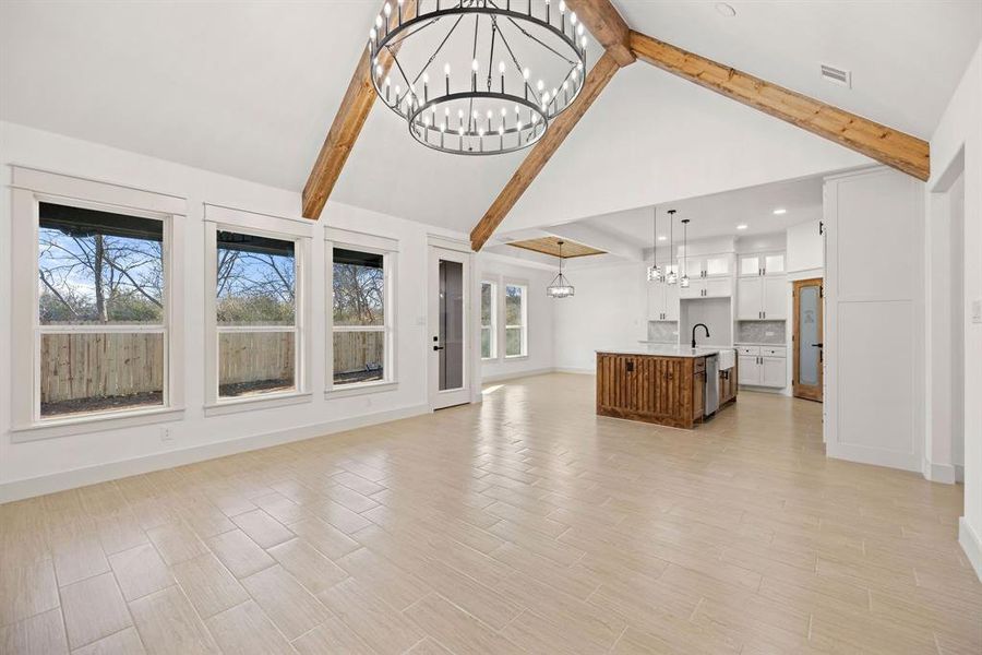 Unfurnished living room featuring light wood finished floors, visible vents, beamed ceiling, a notable chandelier, and a sink