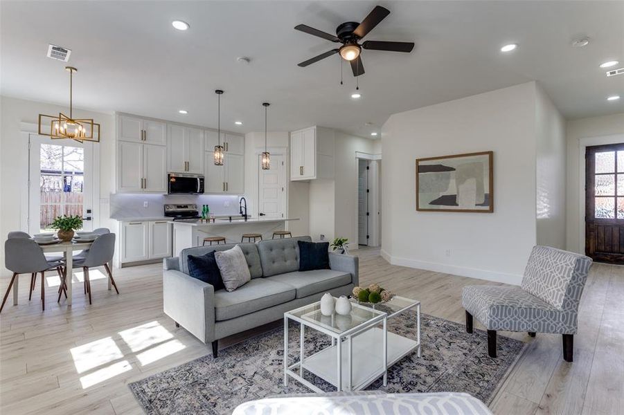 Living area featuring visible vents, baseboards, recessed lighting, light wood-style floors, and ceiling fan with notable chandelier