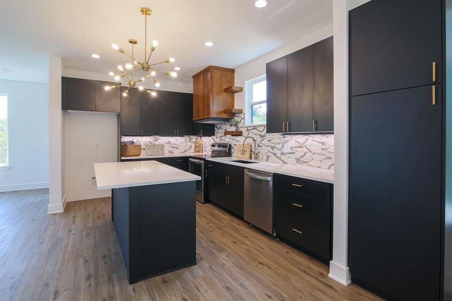 Kitchen with light wood-type flooring, a center island, hanging light fixtures, decorative backsplash, and appliances with stainless steel finishes