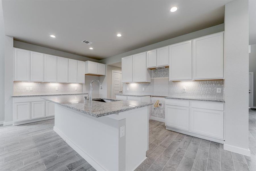 Culinary haven, featuring granite countertops, a tile backsplash, stainless steel appliances, 42” upper cabinets, and undercabinet lighting. Sample photo of completed home with similar floor plan. As-built interior colors and selections may vary.