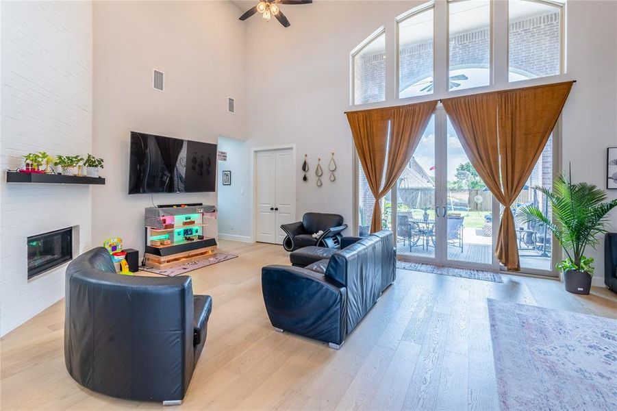 Living room featuring light wood-style flooring, a fireplace, french doors, a ceiling fan, and a high ceiling