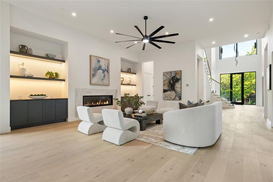 Spacious living area featuring light wood-finish flooring, a contemporary fireplace with a stone surround, and built-in shelving with integrated lighting Spacious living area featuring light wood-finish flooring, a contemporary fireplace with a stone surround, and built-in shelving with integrated lighting