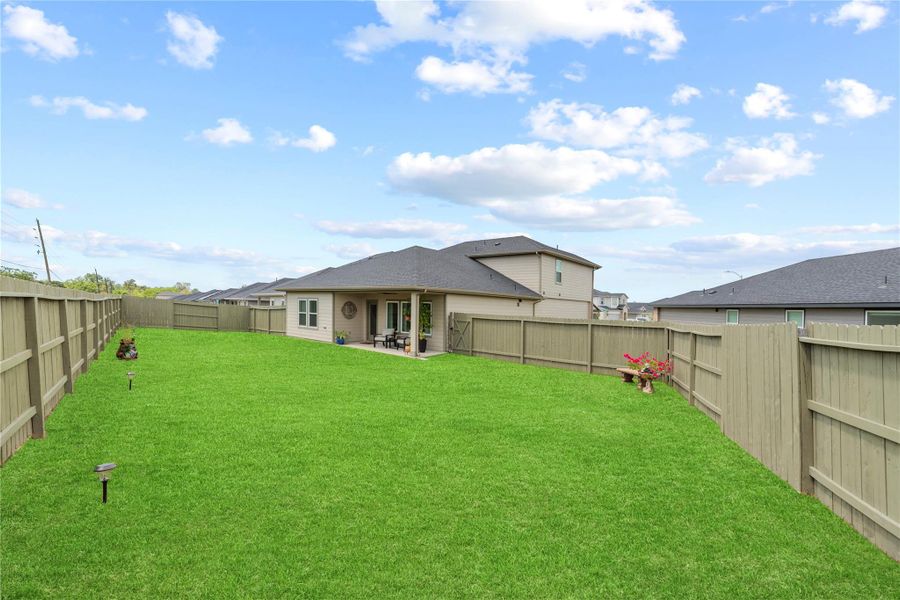 Large fenced backyard with a lush lawn and covered patio, with space for outdoor dining and play.