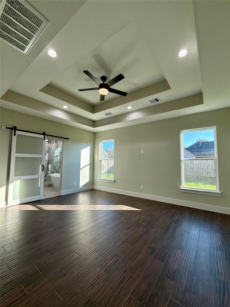 This spacious room features elegant dark wood tile floors, a tray ceiling with recessed lighting, and a modern ceiling fan. It has abundant natural light from two large windows and includes a sliding barn door leading to a Spa like bathroom. This spacious room features elegant dark wood tile floors, a tray ceiling with recessed lighting, and a modern ceiling fan. It has abundant natural light from two large windows and includes a sliding barn door leading to a Spa like bathroom.