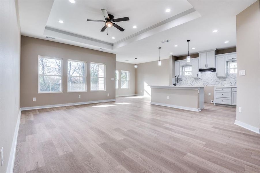 Unfurnished living room featuring visible vents, light wood-style floors, a tray ceiling, and a sink