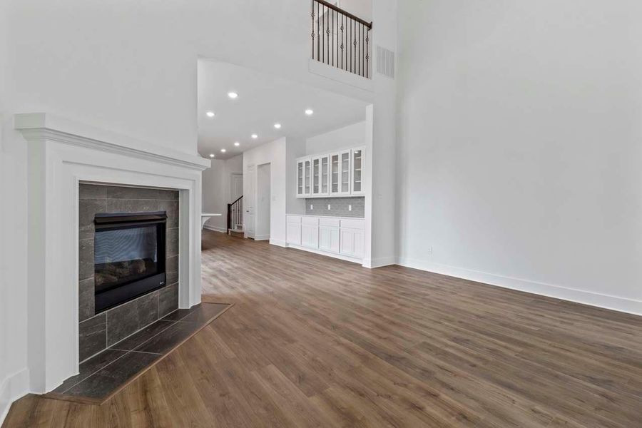 Unfurnished living room with a fireplace, recessed lighting, dark wood-style flooring, a towering ceiling, and stairs Unfurnished living room with a fireplace, recessed lighting, dark wood-style flooring, a towering ceiling, and stairs