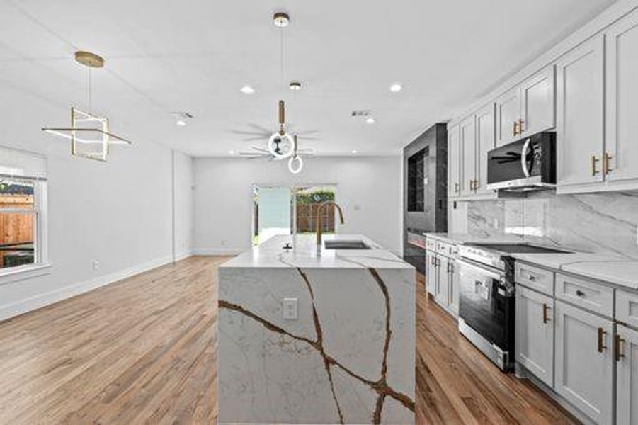 Kitchen with light stone countertops, stainless steel appliances, decorative light fixtures, and wood-type flooring