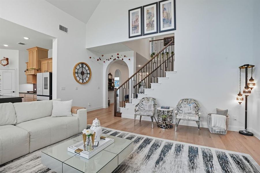 Living room featuring light wood-style flooring, recessed lighting, arched walkways, high vaulted ceiling, and stairway