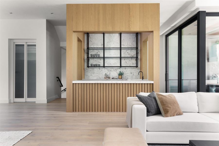 Indoor wet bar featuring modern cabinets, light wood finished floors, backsplash, and light wood finish cabinetry
