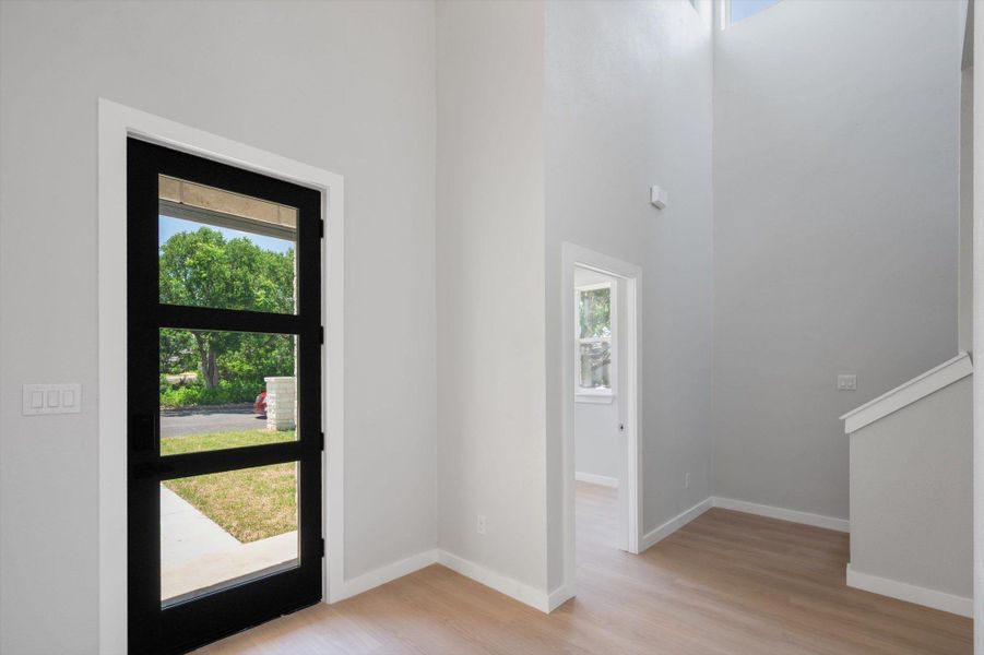 A tall ceiling entrance offers a welcoming pathway with light wood flooring leading to the interior.