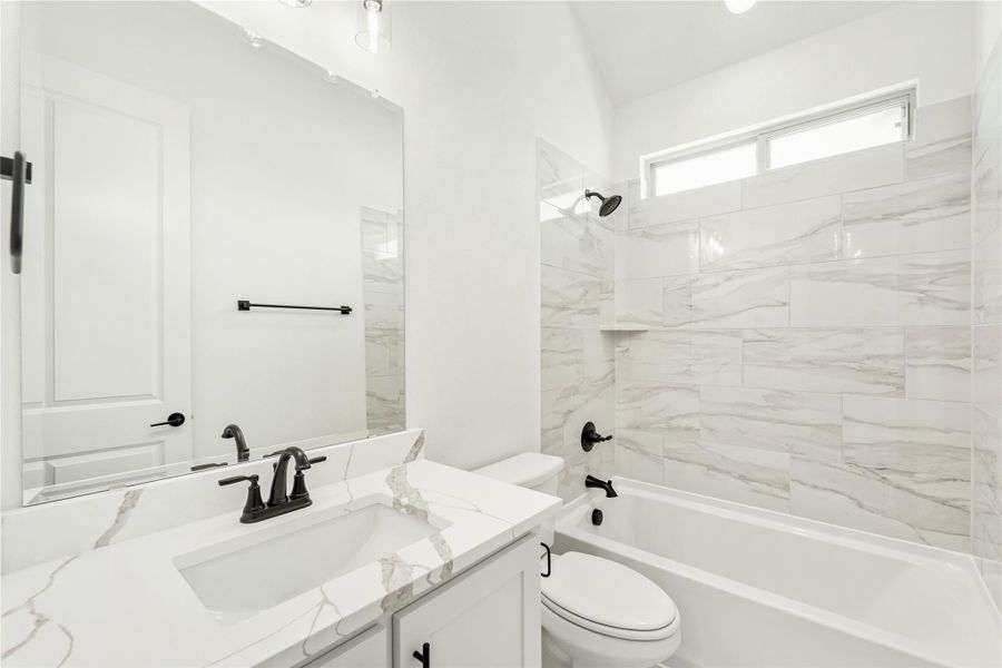 Bathroom with marble-look tile, white quartz vanity, black fixtures, and tub-shower combo with tiled surround.
