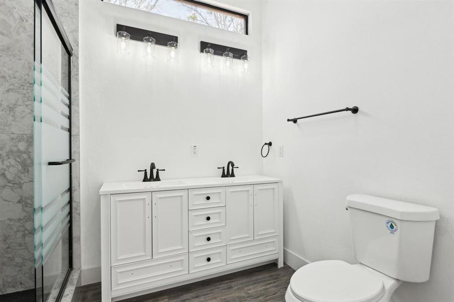 Full bath featuring a sink, a shower stall, toilet, and wood finished floors