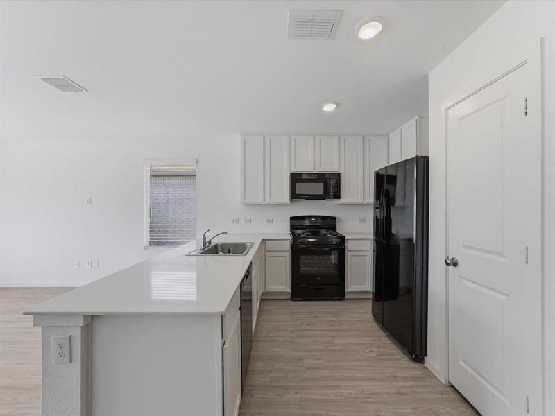 Open-concept kitchen featuring white cabinetry, light-toned countertops, and wood-finish flooring