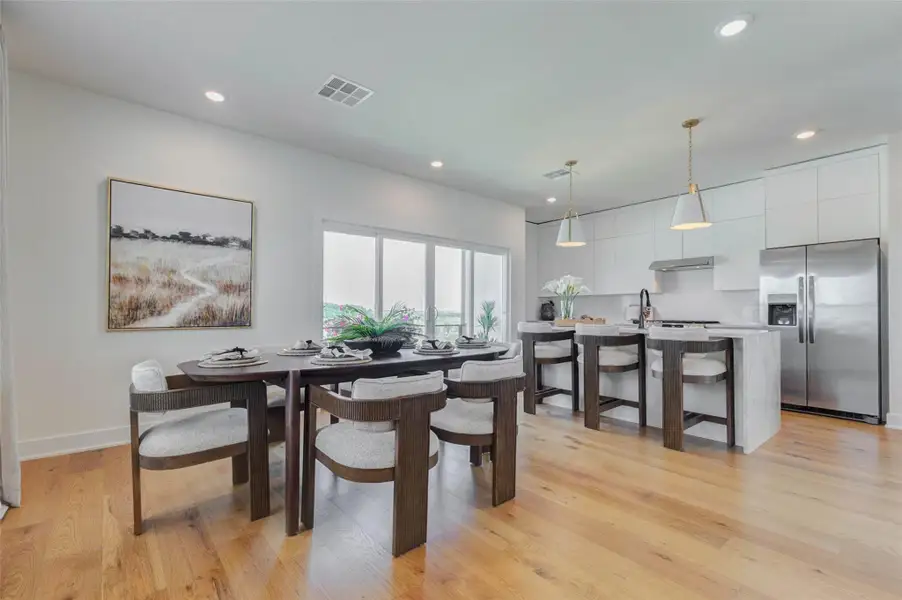 The dining area and kitchen combine modern design with everyday functionality. A generous dining table offers seating for six, while the waterfall-edge island adds additional seating, prep space, and visual impact. Ceiling-height cabinetry, stainless-steel appliances, pendant lighting, and warm wood floors create a polished contemporary look. Oversized sliding doors fill the space with natural light and connect directly to the outdoor balcony.