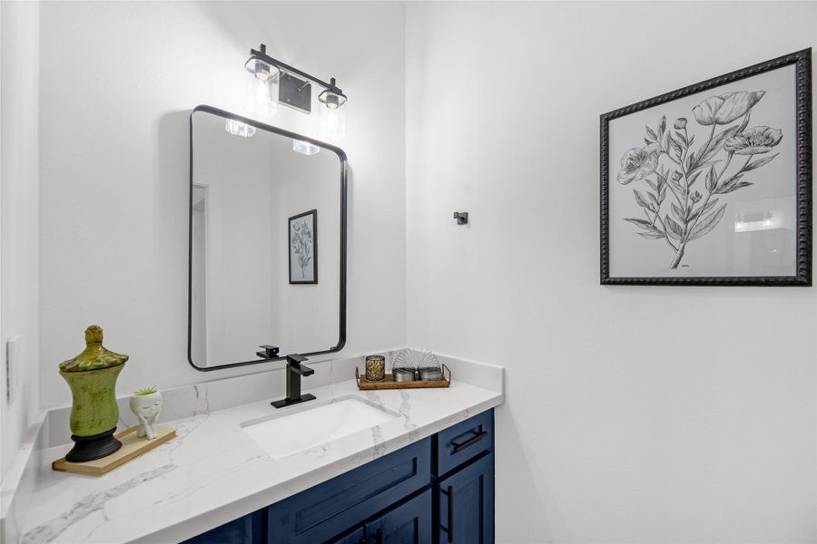 Sleek, white marble countertop and deep blue cabinetry. It features a rectangular black-framed mirror and stylish lighting above.