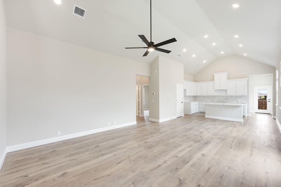 Open living area with vaulted ceiling, ceiling fan, wood floors, and white kitchen with island in background