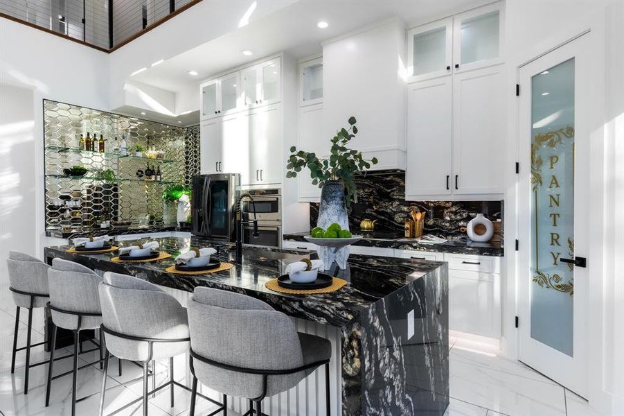 Kitchen with dark granite countertops, glass insert cabinets, a kitchen bar, a center island with sink, and white cabinets Kitchen with dark granite countertops, glass insert cabinets, a kitchen bar, a center island with sink, and white cabinets