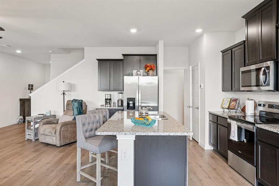 Kitchen with stainless steel appliances, a kitchen bar, recessed lighting, light wood-type flooring, and light stone countertops Kitchen with stainless steel appliances, a kitchen bar, recessed lighting, light wood-type flooring, and light stone countertops