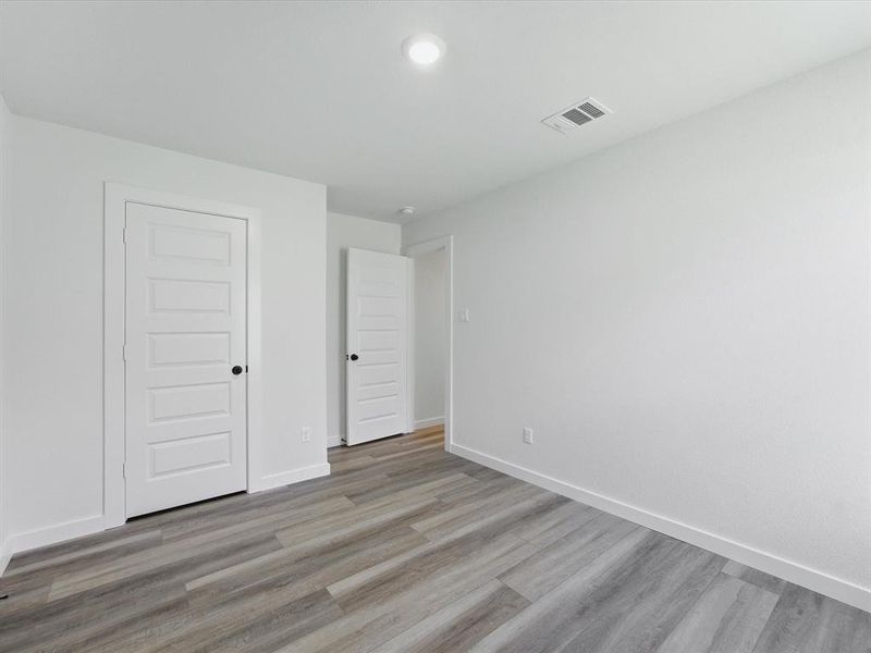 Interior room featuring wood-finish flooring, white walls, and bright overhead lighting Interior room featuring wood-finish flooring, white walls, and bright overhead lighting