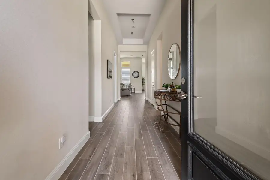 This entryway features a sleek, modern design with wood-look tile flooring and neutral walls. A decorative console table with a mirror adds elegance, and the space is well-lit, leading into a cozy living area. This entryway features a sleek, modern design with wood-look tile flooring and neutral walls. A decorative console table with a mirror adds elegance, and the space is well-lit, leading into a cozy living area.