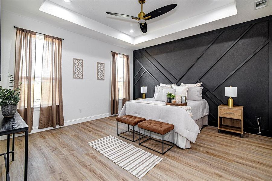 Bedroom with a raised ceiling, light wood-type flooring, and a ceiling fan