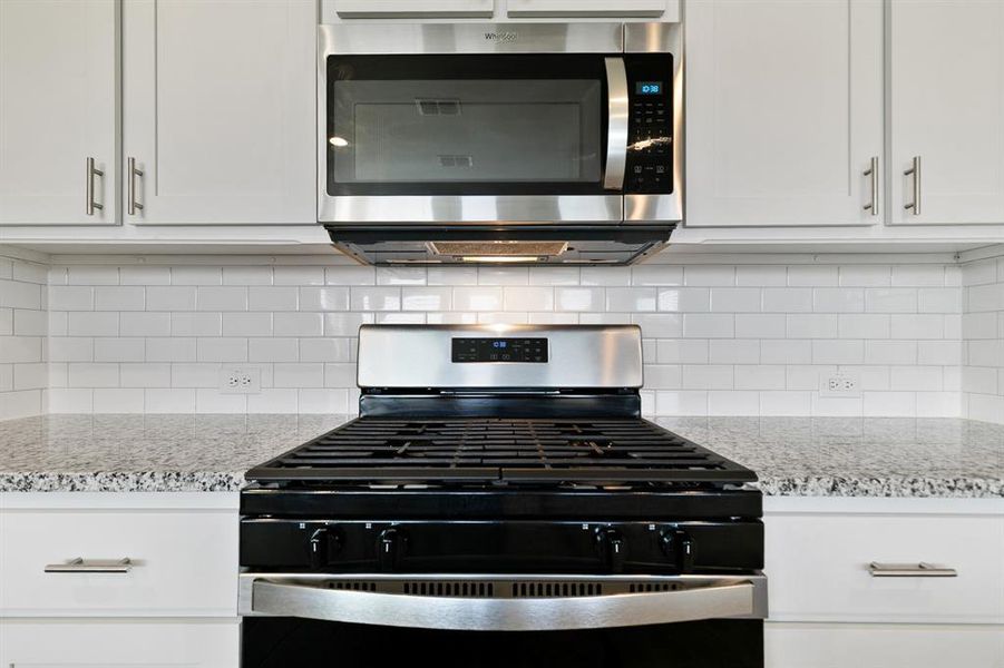 Kitchen with appliances with stainless steel finishes, light stone countertops, and white cabinetry