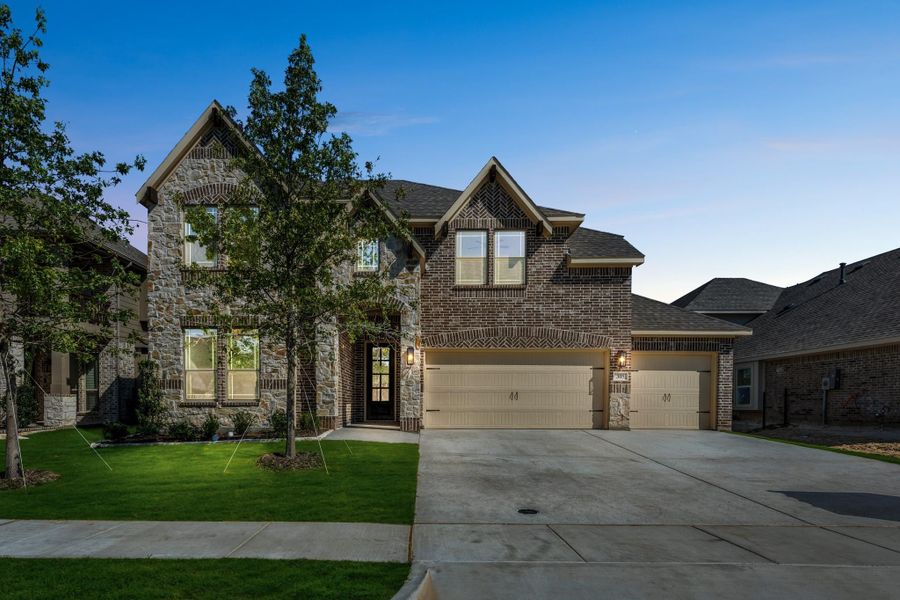 Two-story brick and stone home with three-car garage, arched entry, and manicured front lawn