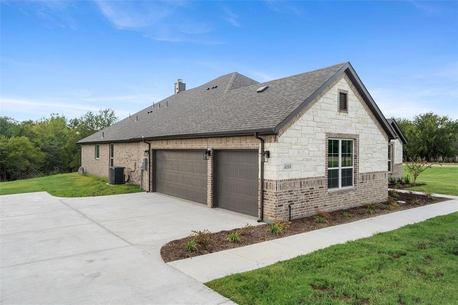 View of home's exterior with a yard, roof with shingles, a garage, brick siding, and driveway
