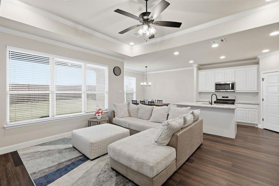 Living area with dark wood finished floors, a chandelier, recessed lighting, crown molding, and a ceiling fan