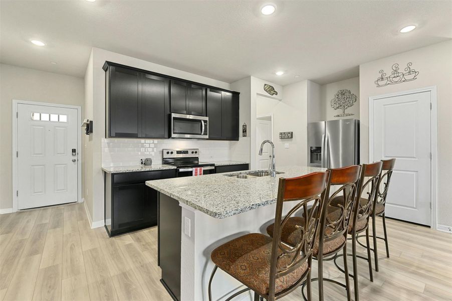 Kitchen with sink, light stone counters, a breakfast bar, an island with sink, and stainless steel appliances