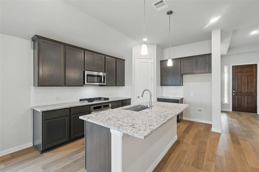 Kitchen featuring a sink, appliances with stainless steel finishes, light stone counters, light wood-type flooring, and tasteful backsplash Kitchen featuring a sink, appliances with stainless steel finishes, light stone counters, light wood-type flooring, and tasteful backsplash