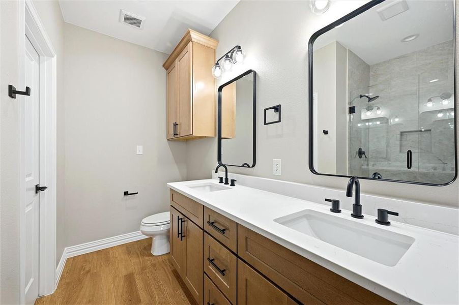 Full bathroom featuring a shower stall, double vanity, and light wood-style floors Full bathroom featuring a shower stall, double vanity, and light wood-style floors