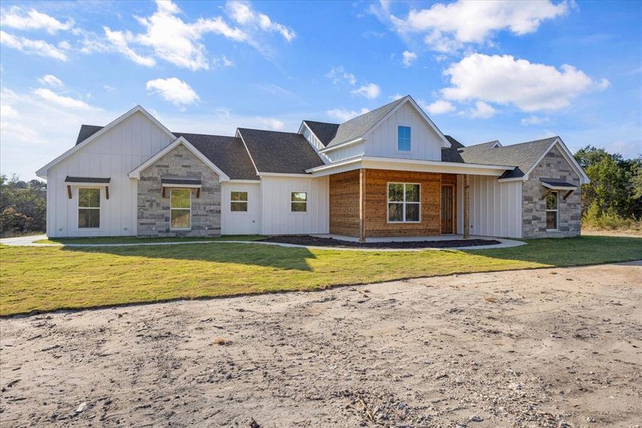 Modern farmhouse style home featuring board and batten siding, stone siding, and a front lawn