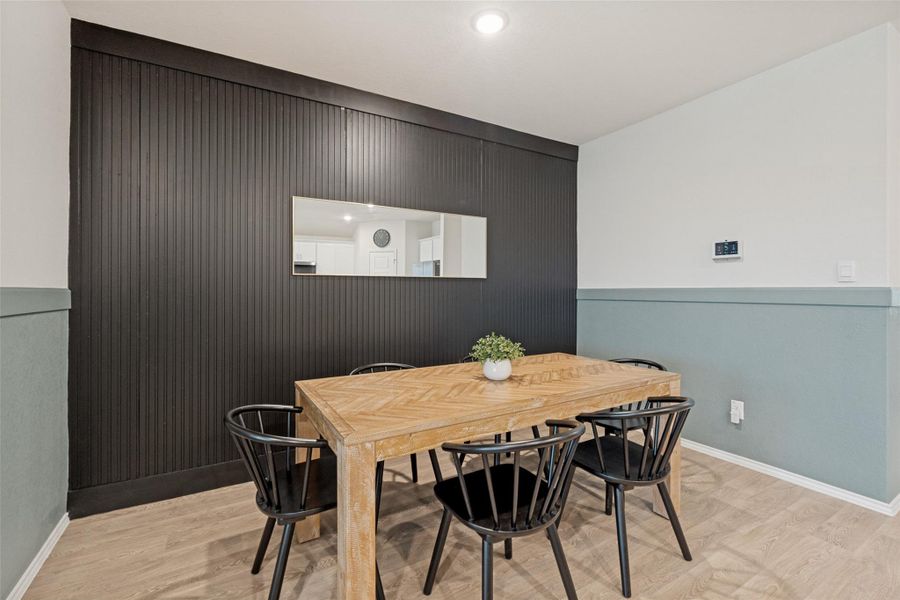 A well-lit dining area featuring a light wood table, accented by a dark wood-paneled wall, creating an inviting space for gatherings.