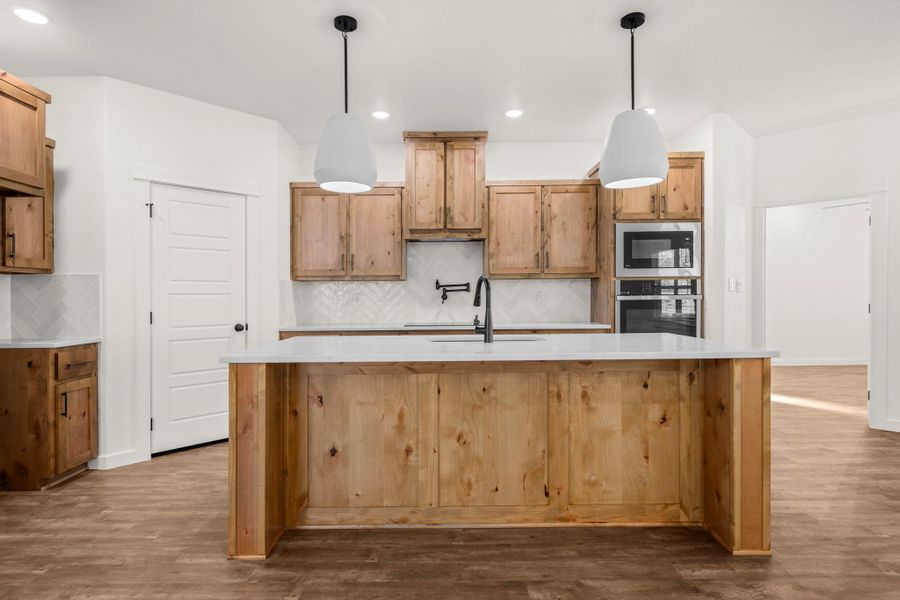 An inviting kitchen with a spacious island, pendant lights, and light wood cabinetry.