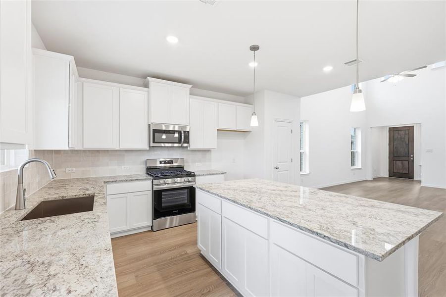 Kitchen with stainless steel appliances, a center island, light wood-type flooring, hanging light fixtures, and white cabinetry