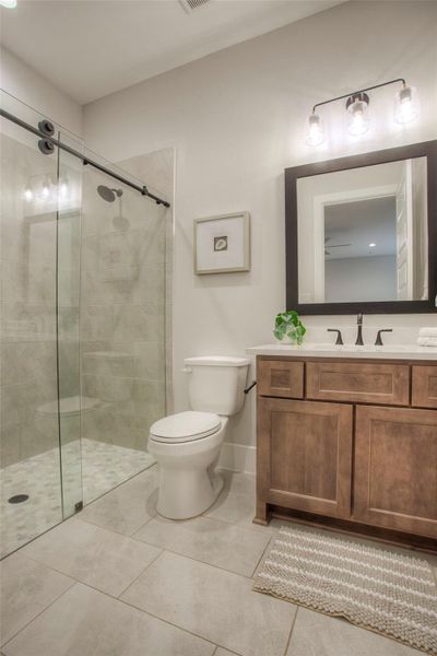 This bathroom features a modern design with a spacious walk-in shower, glass sliding doors, and sleek tile work. It includes a wooden vanity with a large mirror and elegant lighting.