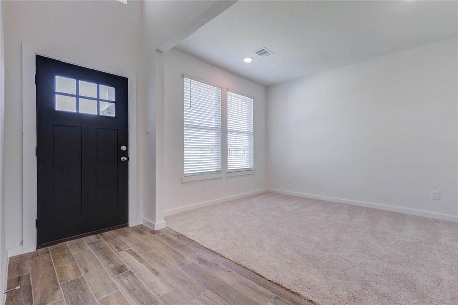 Welcoming entry area with a bold black front door, window panel detail, wood-look tile flooring, and a bright adjacent flex space. The soft neutral walls and natural light create a clean, airy first impression. This front room could function beautifully as a formal dining area, sitting room, study, or versatile space tailored to the buyer’s lifestyle. Welcoming entry area with a bold black front door, window panel detail, wood-look tile flooring, and a bright adjacent flex space. The soft neutral walls and natural light create a clean, airy first impression. This front room could function beautifully as a formal dining area, sitting room, study, or versatile space tailored to the buyer’s lifestyle.
