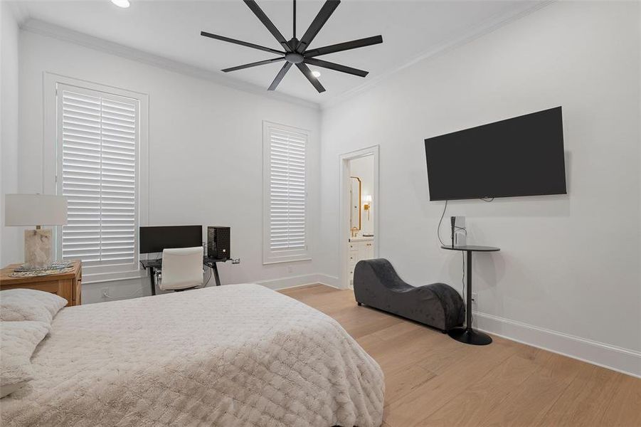 Bedroom featuring light wood-style floors, crown molding, a ceiling fan, and ensuite bath