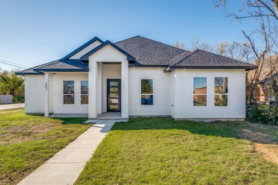 View of front of property with roof with shingles, a front lawn, and stucco siding