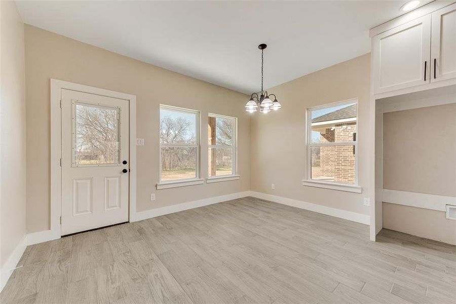 Unfurnished dining area with a wealth of natural light, a notable chandelier, and light wood-type flooring