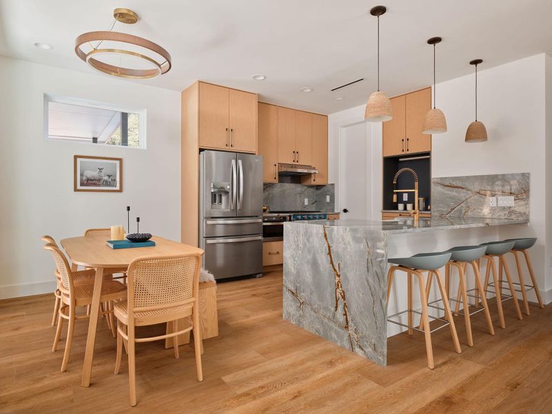 Kitchen with light brown cabinets, decorative backsplash, decorative light fixtures, light stone counters, and stainless steel fridge with ice dispenser Kitchen with light brown cabinets, decorative backsplash, decorative light fixtures, light stone counters, and stainless steel fridge with ice dispenser