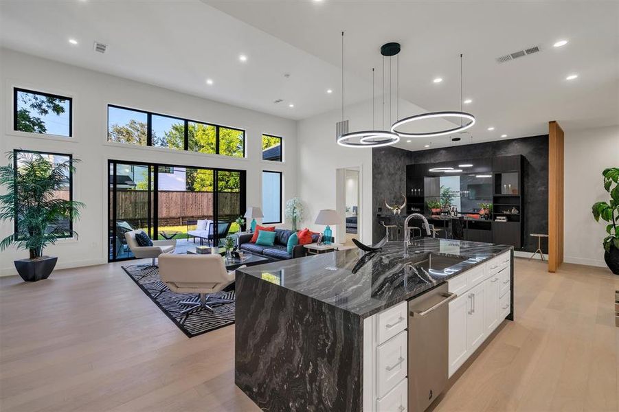 Kitchen with a high ceiling, dark stone counters, hanging light fixtures, white cabinetry, and a large island