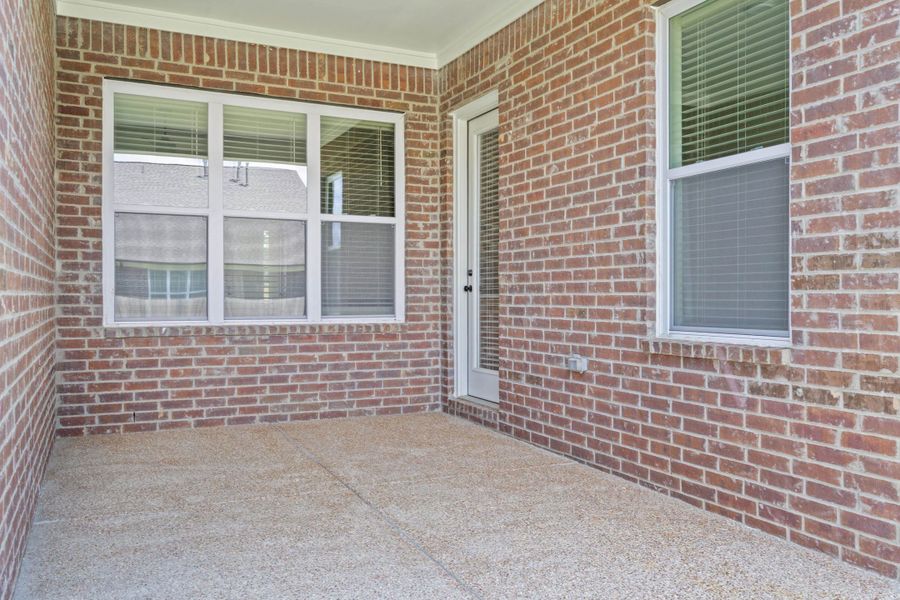 Covered patio featuring a durable aggregate concrete surface, red brick exterior walls, multiple white-framed windows, and a glass-paneled door Covered patio featuring a durable aggregate concrete surface, red brick exterior walls, multiple white-framed windows, and a glass-paneled door