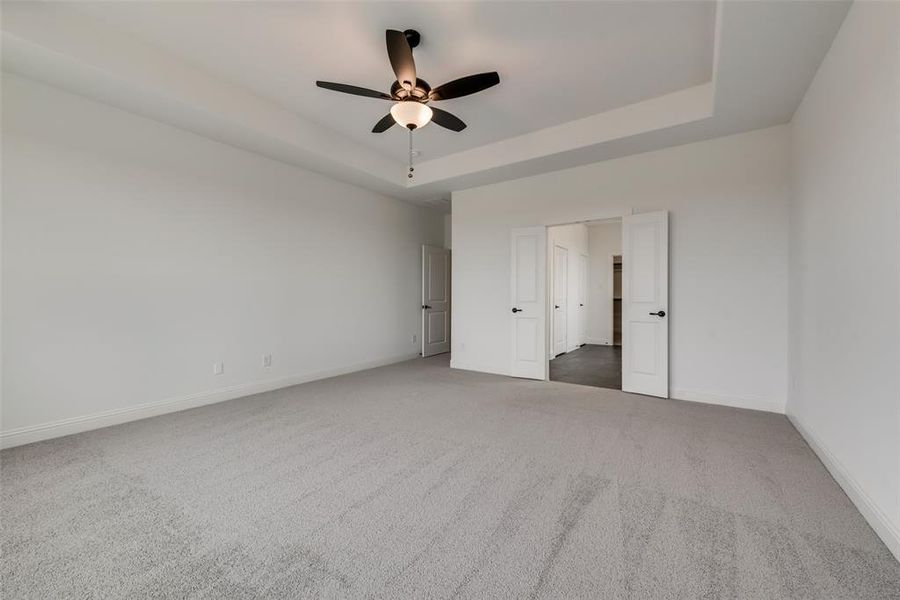 Unfurnished bedroom with ceiling fan, a tray ceiling, and dark carpet