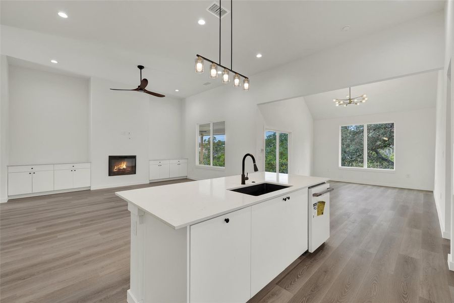 Kitchen with open floor plan, a glass covered fireplace, white cabinets, light wood-type flooring, and recessed lighting