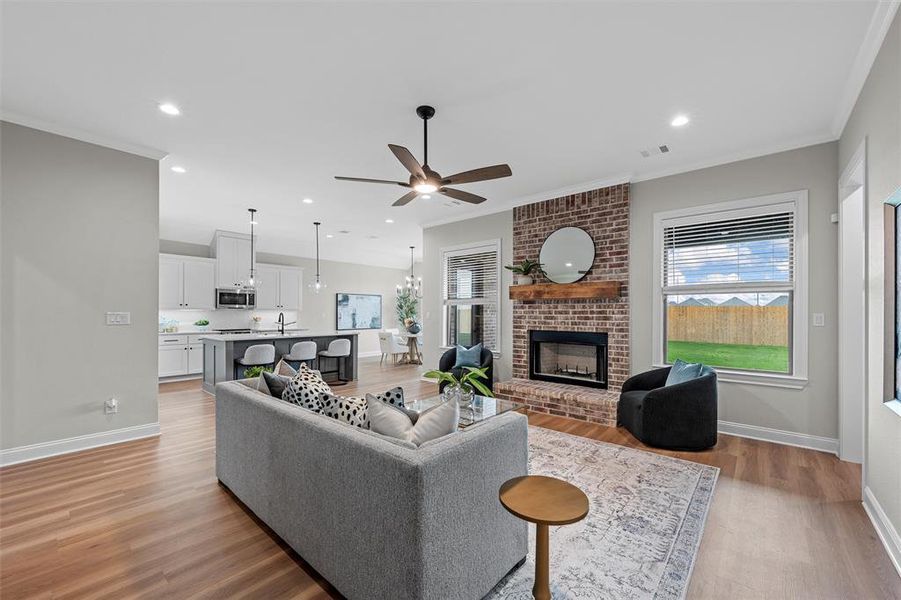 Living area featuring crown molding, light wood finished floors, a fireplace, ceiling fan, and a chandelier Living area featuring crown molding, light wood finished floors, a fireplace, ceiling fan, and a chandelier