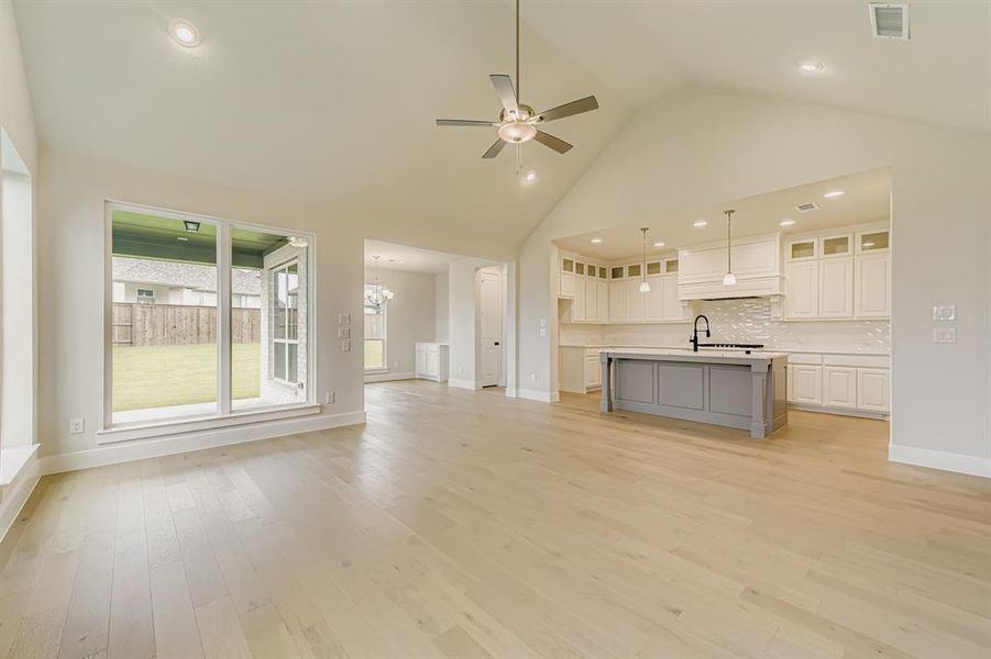 Unfurnished living room with high vaulted ceiling, a ceiling fan, light wood-style floors, a chandelier, and recessed lighting