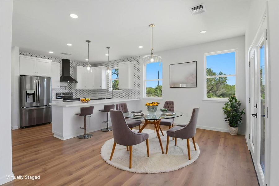 Open-concept kitchen and dining area featuring white cabinetry, stainless steel appliances, and wood-finish flooring Open-concept kitchen and dining area featuring white cabinetry, stainless steel appliances, and wood-finish flooring